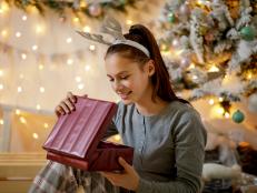 Happy teenage girl in pajamas and antler headband opening Christmas present