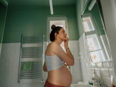 Photo of a young pregnant woman getting ready in the bathroom for the upcoming day; applying moisturizer as a part of her daily routine.