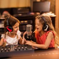 Two small girls having fun in a radio station while talking on a microphone.