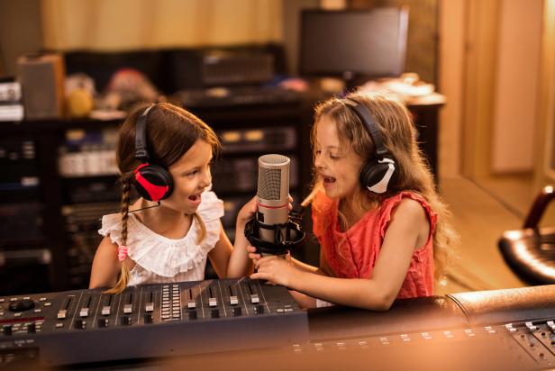 Two small girls having fun in a radio station while talking on a microphone.