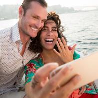 Couple takes engagement selfie on a sailboat.