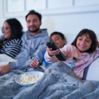 Family relaxing on living room sofa and watching TV with popcorn at night
