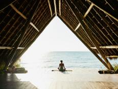 Wide shot of woman relaxing after practicing yoga in ocean front pavilion at tropical resort