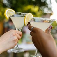 Close up shot of two unrecognizable, diverse girlfriends cheering with martini glasses with margarita cocktails during a summer garden party.