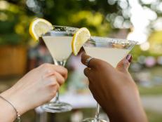 Close up shot of two unrecognizable, diverse girlfriends cheering with martini glasses with margarita cocktails during a summer garden party.