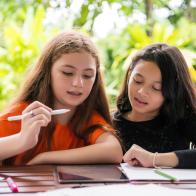 E-learning. Young cute little girls sitting at a desk. Using digital tablet are working on their school homework having fun.