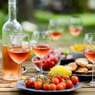 Table apéro pique-nique à l'exterieur le soir dans le jardin en été, avec du vin rosé, boissons fraiches, charcuteries, biscuits apéritifs et divers légumes. / Holiday summer brunch party table outdoor in house backyard with appetizer, glass of rosé wine, fresh drink and organic vegetables.