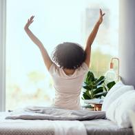 Shot of a young woman sitting on the bed in the morning and stretching