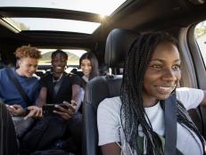 Happy teenage girl driving friends riding in back seat, using smart phone in car with sunroof