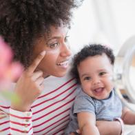 Mother holding baby son applying face cream in mirror