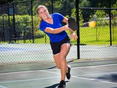A Caucasian young  adult woman pickleball player in action. She is holding a pickleball paddle posing to return the ball in a pickleball court. Photographed in horizontal format with copy space.