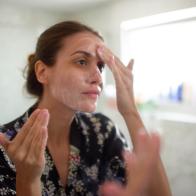 Young female in the bathroom looking in the mirror and taking care of her facial skin.