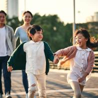 happy asian family with two children walking on pedestrian bridge in city park