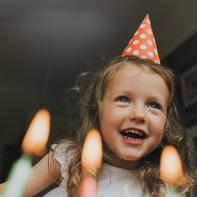 Portrait of a happy and excited pre-school age child, wearing a spotty party hat, above a birthday cake in anticipation of blowing out the coloured candles. Image taken at an unusual low angle giving an unexpected perspective. Space for copy.