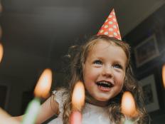 Portrait of a happy and excited pre-school age child, wearing a spotty party hat, above a birthday cake in anticipation of blowing out the coloured candles. Image taken at an unusual low angle giving an unexpected perspective. Space for copy.