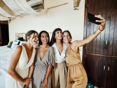 Medium wide shot of smiling and laughing bridesmaids tasking selfie in luxury hotel suite before wedding