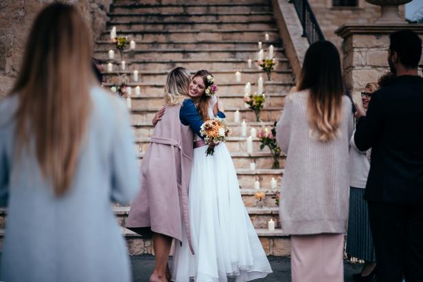 Loving mother embracing elegant bride at outdoors rustic cottage wedding ceremony in Europe