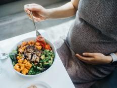 Cropped shot of pregnant woman gently touching her belly, eating fresh and healthy multi-coloured vegetable salad bowl. Eating well with balanced nutrition. Healthy eating habit and lifestyle during pregnancy