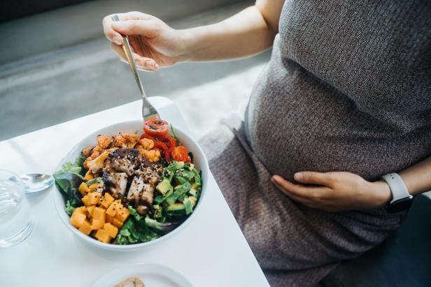 Cropped shot of pregnant woman gently touching her belly, eating fresh and healthy multi-coloured vegetable salad bowl. Eating well with balanced nutrition. Healthy eating habit and lifestyle during pregnancy