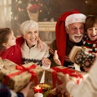 Happy senior grandparents and their small grandkids receiving Christmas presents at dining table. 