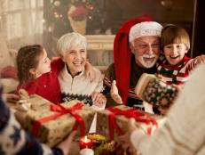 Happy senior grandparents and their small grandkids receiving Christmas presents at dining table. 