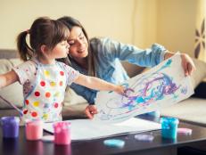 A young mother and her cute little daughter painting with colorful paints and having fun at home.