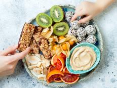 Mother sharing healthy vegan dessert snacks with toddler child. Concept of healthy sweets for children. Protein granola bars, homemade raw energy balls, cashew butter, toasted coconut chips, fruits platter