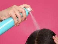Young woman applying dry shampoo against pink background, closeup