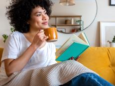 Pensive relaxed African american woman reading a book at home, drinking coffee sitting on the couch. Copy space. Lifestyle concept.