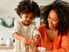 African American woman with her little daughter with curly fluffy hair having fun and making pastries in the kitchen. Mom and daughter cooking together.
