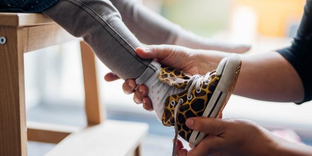 Closeup of young Asian mom helping her little girl to put on shoes, preparing to go to nursery school. Family bonding time. Love and care concept.