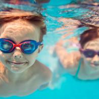 Smiling kids enjoying underwater swim in the pool towards the camera. Sunny summer day. Brother aged 5 is in the front, the sister is aged 9 and is swimming in the background. Slightly soft.