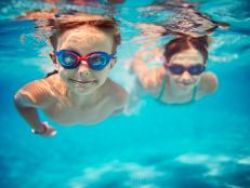 Smiling kids enjoying underwater swim in the pool towards the camera. Sunny summer day. Brother aged 5 is in the front, the sister is aged 9 and is swimming in the background. Slightly soft.