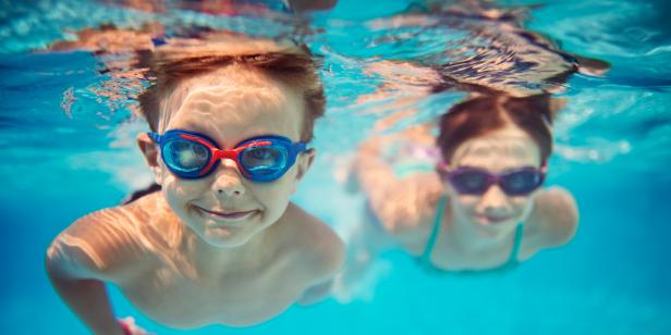 Smiling kids enjoying underwater swim in the pool towards the camera. Sunny summer day. Brother aged 5 is in the front, the sister is aged 9 and is swimming in the background. Slightly soft.