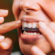 Woman using teeth whitening strips at home.