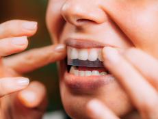 Woman using teeth whitening strips at home.