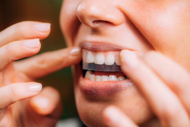 Woman using teeth whitening strips at home.