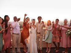 Portrait of happy just married couple and guests toasting drinks while standing against sky at sunset