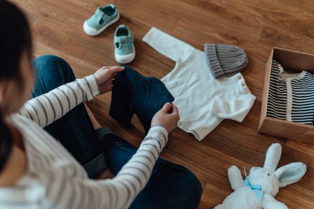 High angle shot of pregnant woman unpacking parcel of baby clothing from online shopping. Baby goods laying on the floor. Getting ready for a new born!