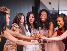 A happy group of diverse adult female friends toasting to their Latin friend who is about to get married soon. They are all cheering and looking excited. The girls are dressed in fancy dresses and are located in a luxurious apartment.