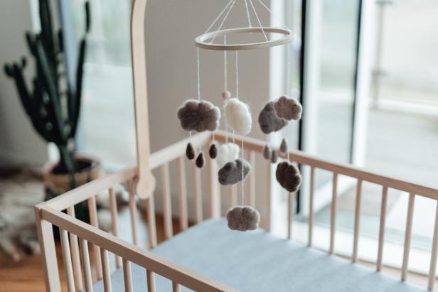 Stylish Scandinavian newborn baby nursery with natural wooden baby cot and handmade mobile hanging over it. Modern interior with white coloured walls, wooden furniture and indoor plants in the morning daylight. Getting ready for a new born! Welcome new born baby concept.