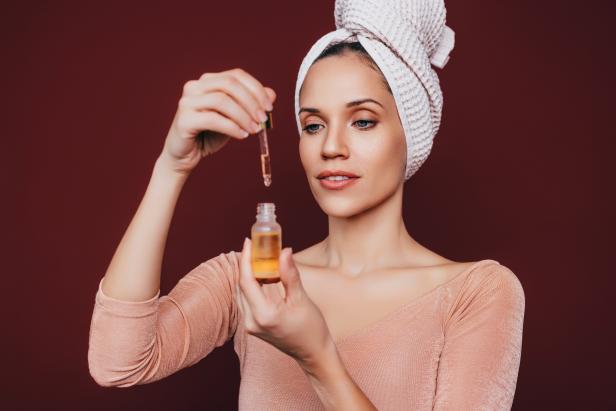 A portrait of a happy woman with her hair wrapped in a towel using jojoba oil for face as part of her skin care routine.