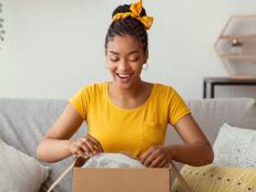 Quick Delivery Service Concept. Happy black lady received package, unpacking cardboard box, sitting on the sofa in living room at home, copy space. Female buyer satisfied with online shopping purchase