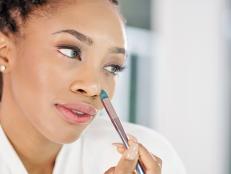 Close-up image of pretty young Black woman appying concealer around her nose to cover red spots