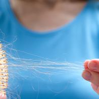 A woman holds a wooden comb in her hands, cleans it of fallen hair after combing. The concept of head health problems, deficient conditions in the body due to stress and depression, a consequence of chemotherapy and radiation for cancer.