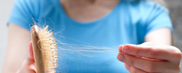 A woman holds a wooden comb in her hands, cleans it of fallen hair after combing. The concept of head health problems, deficient conditions in the body due to stress and depression, a consequence of chemotherapy and radiation for cancer.