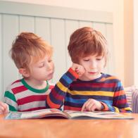 Two young brothers looking at a magazine together while sat at a table.