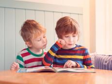 Two young brothers looking at a magazine together while sat at a table.