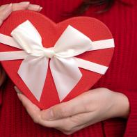 Red heart-shaped gift box with white ribbon in woman's hands, close-up, concept of Valentine's Day present.