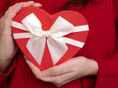 Red heart-shaped gift box with white ribbon in woman's hands, close-up, concept of Valentine's Day present.